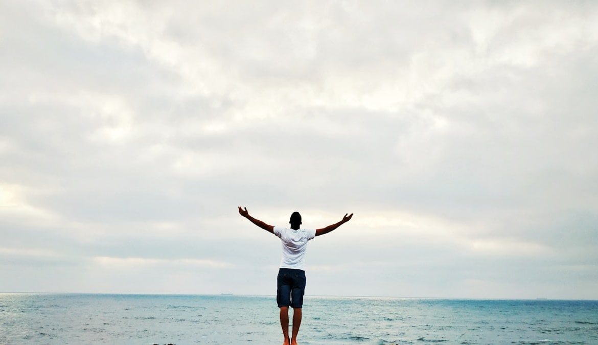 man raising hands standing near seashore during daytime